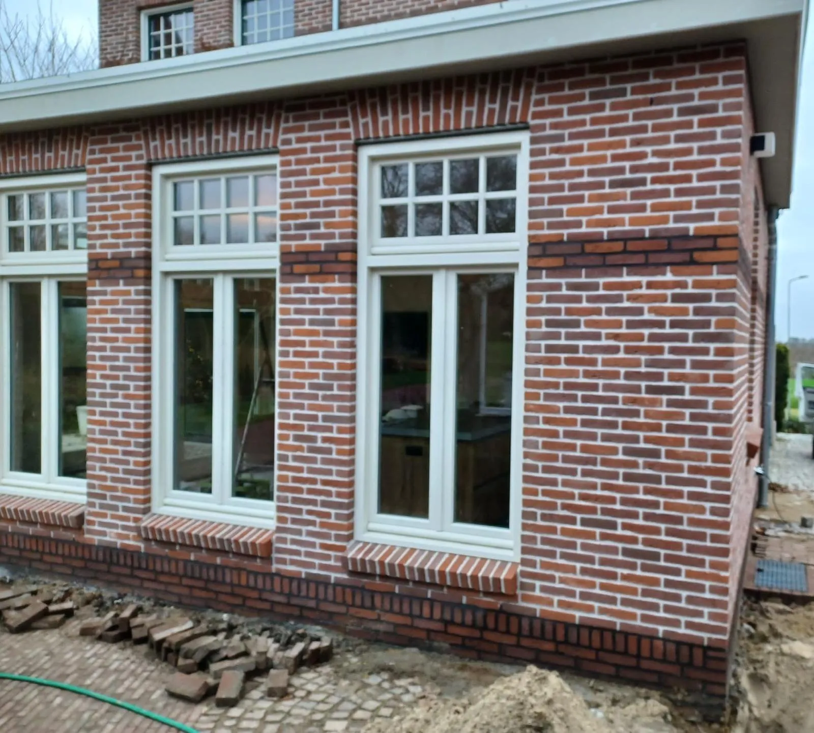 Nieuwe aanbouw in rood metselwerk met gemetselde boogdetails boven witte kozijnen